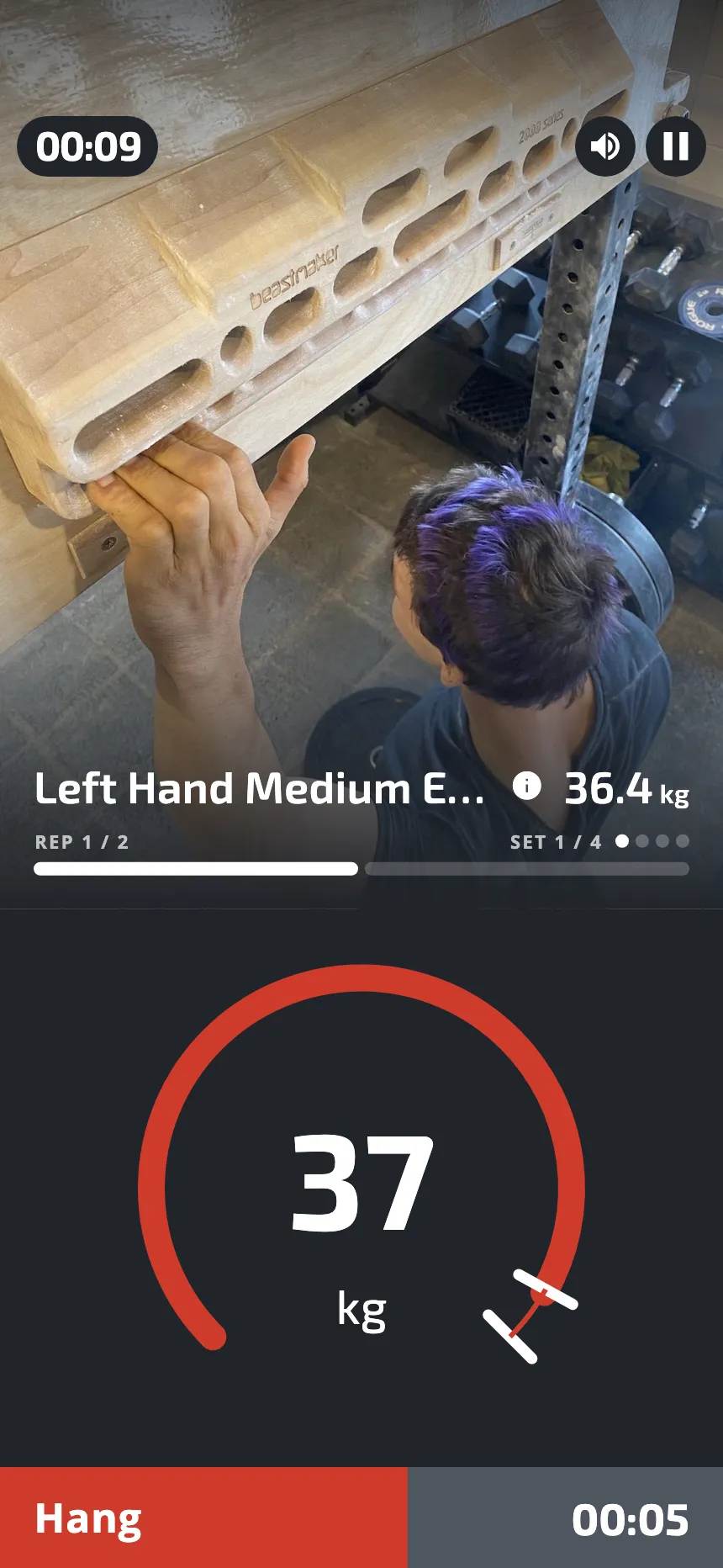 A hang in progress: a climber on a hangboard, and a gauge that shows 37 kg against the target