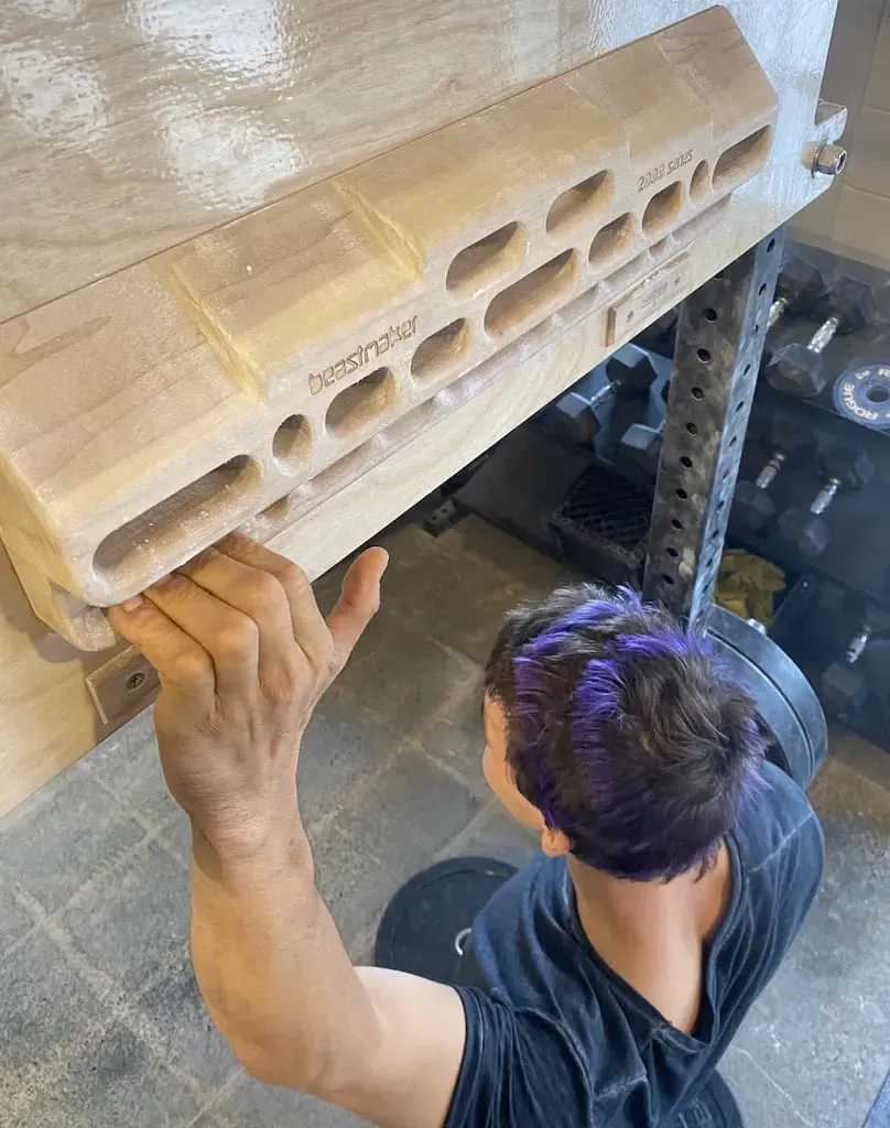 Climber gripping a small edge of a wooden hangboard with one hand