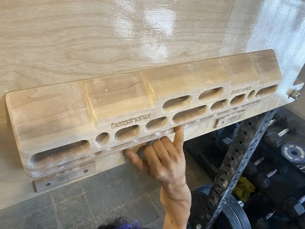 Climber standing under a hangboard and pulling on one edge with one hand