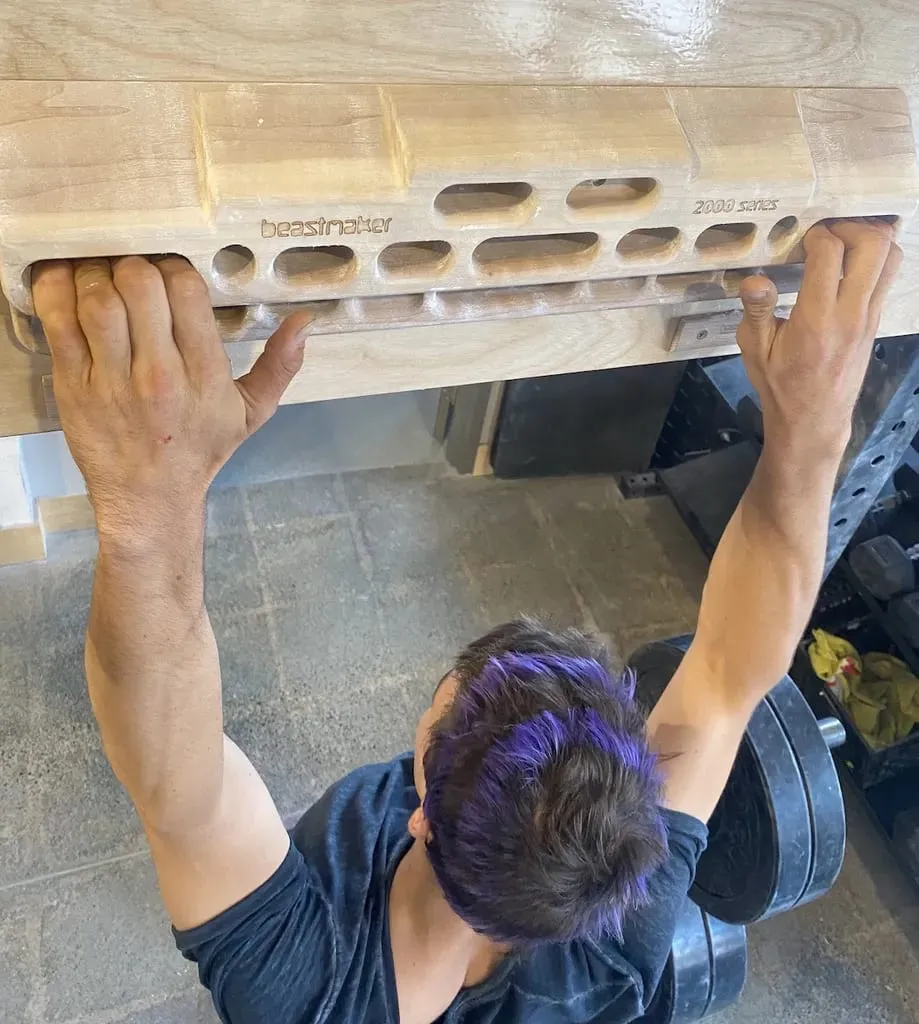 Climber hanging from a medium edge of a wooden hangboard with both hands