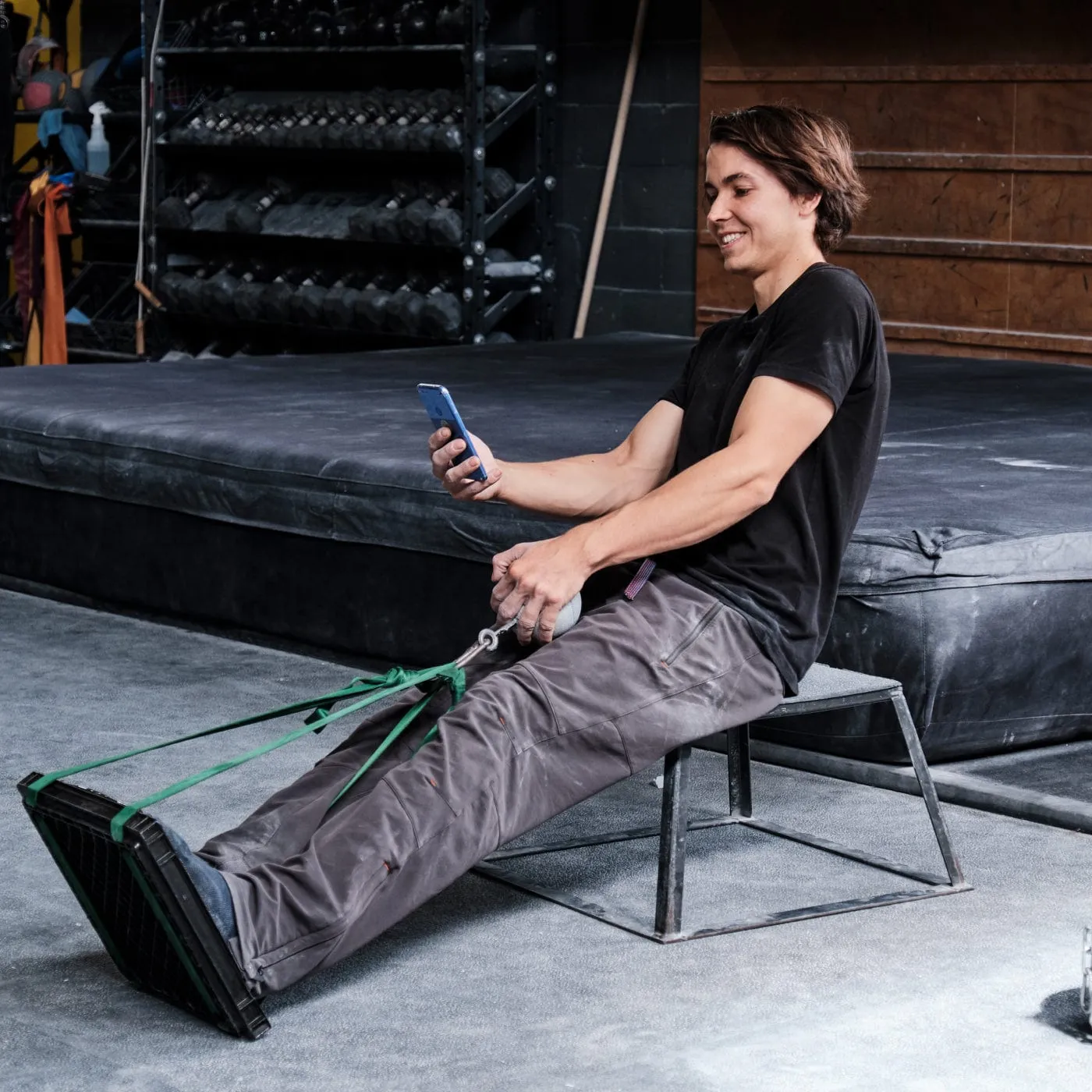 Climber seated on a box, pulling a hold strapped to a plate under the feet while reading the force on a phone